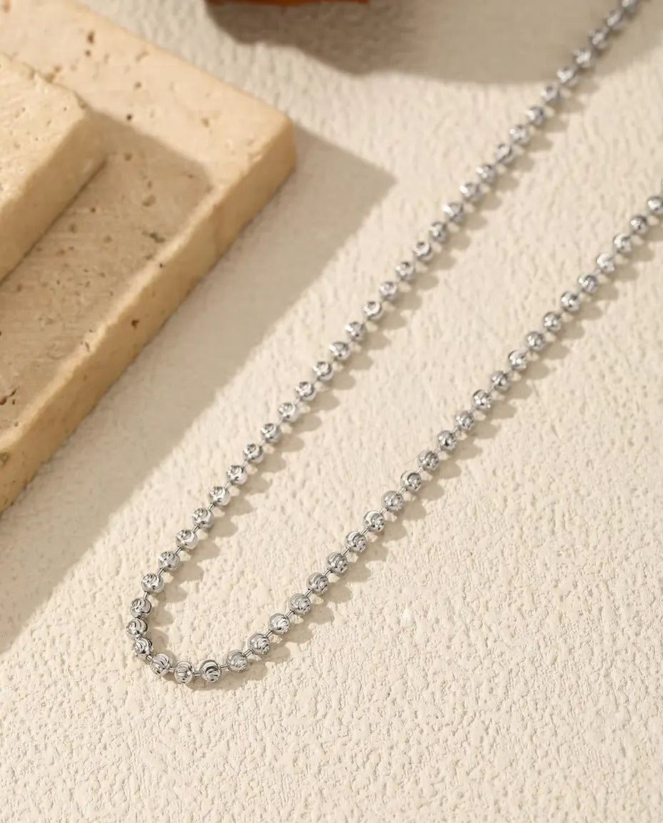 Bead Chain Necklace in 925 Sterling Silver - draped across a cream surface beside a travertine slab