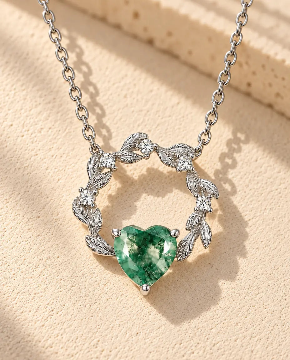 Moss Agate Heart Necklace in 925 Sterling Silver - lying on a cream textured surface beside a travertine block