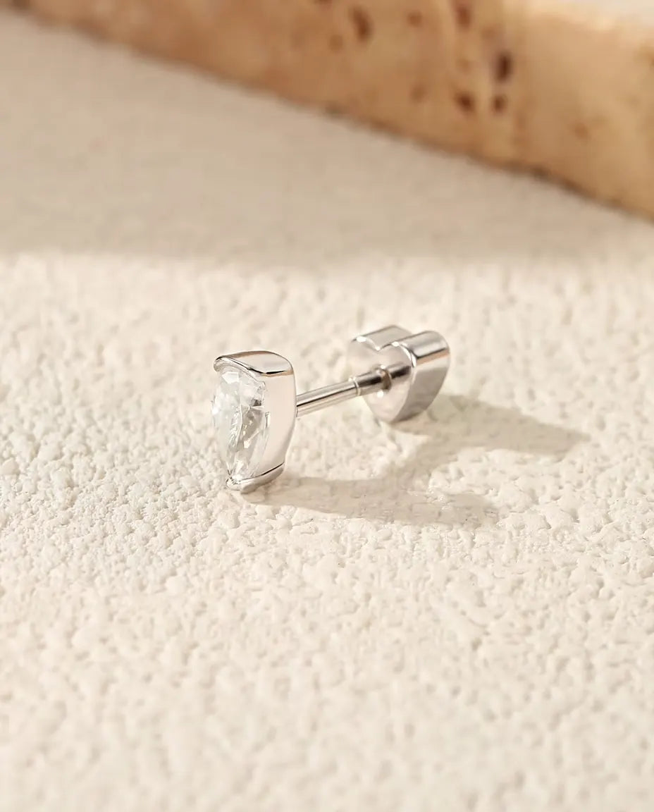 Pear Moissanite Stud Earrings in 925 Sterling Silver - lying on a cream textured surface beside a travertine slab