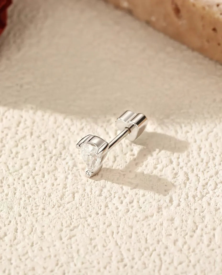 Pear Moissanite Stud Earrings in 925 Sterling Silver - lying on its side on a cream textured surface, heart-shaped back on the post
