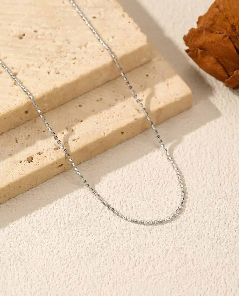 Sparkle Chain Necklace in 925 Sterling Silver - draped across a cream surface beside a travertine slab