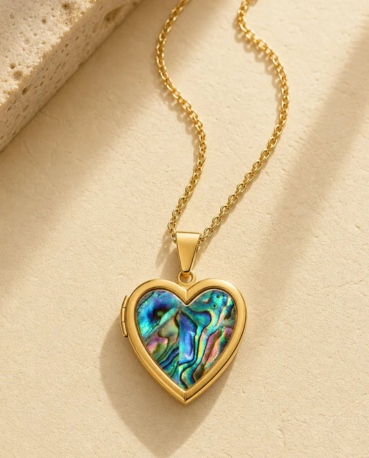 Gold heart locket necklace with iridescent abalone shell front on a warm cream stone surface