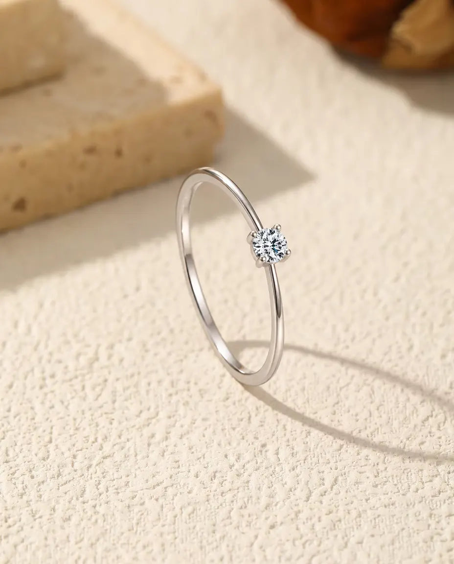Dainty Moissanite Solitaire Ring in 925 Sterling Silver - standing upright on a cream textured surface