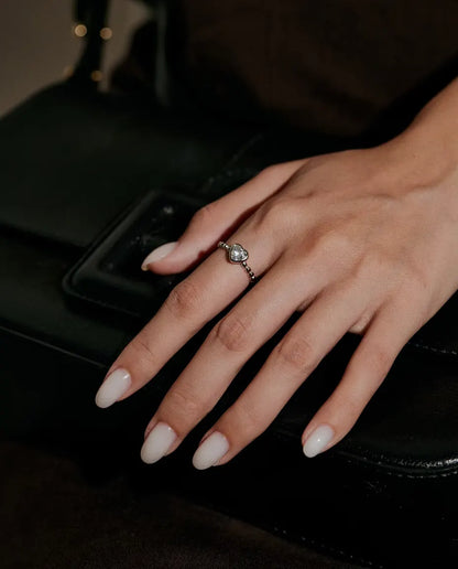 Heart Moissanite Ring in 925 Sterling Silver - worn on a hand resting on a black bag