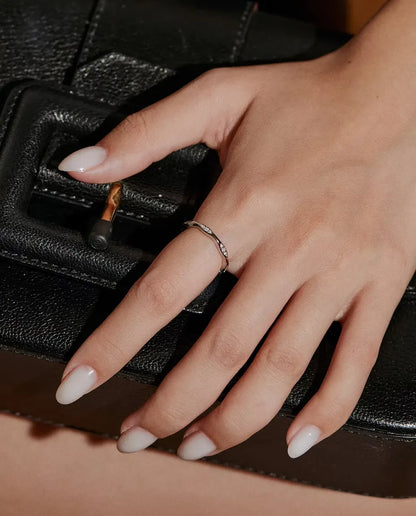 Moissanite Wave Ring in 925 Sterling Silver - worn on a hand resting on a black bag