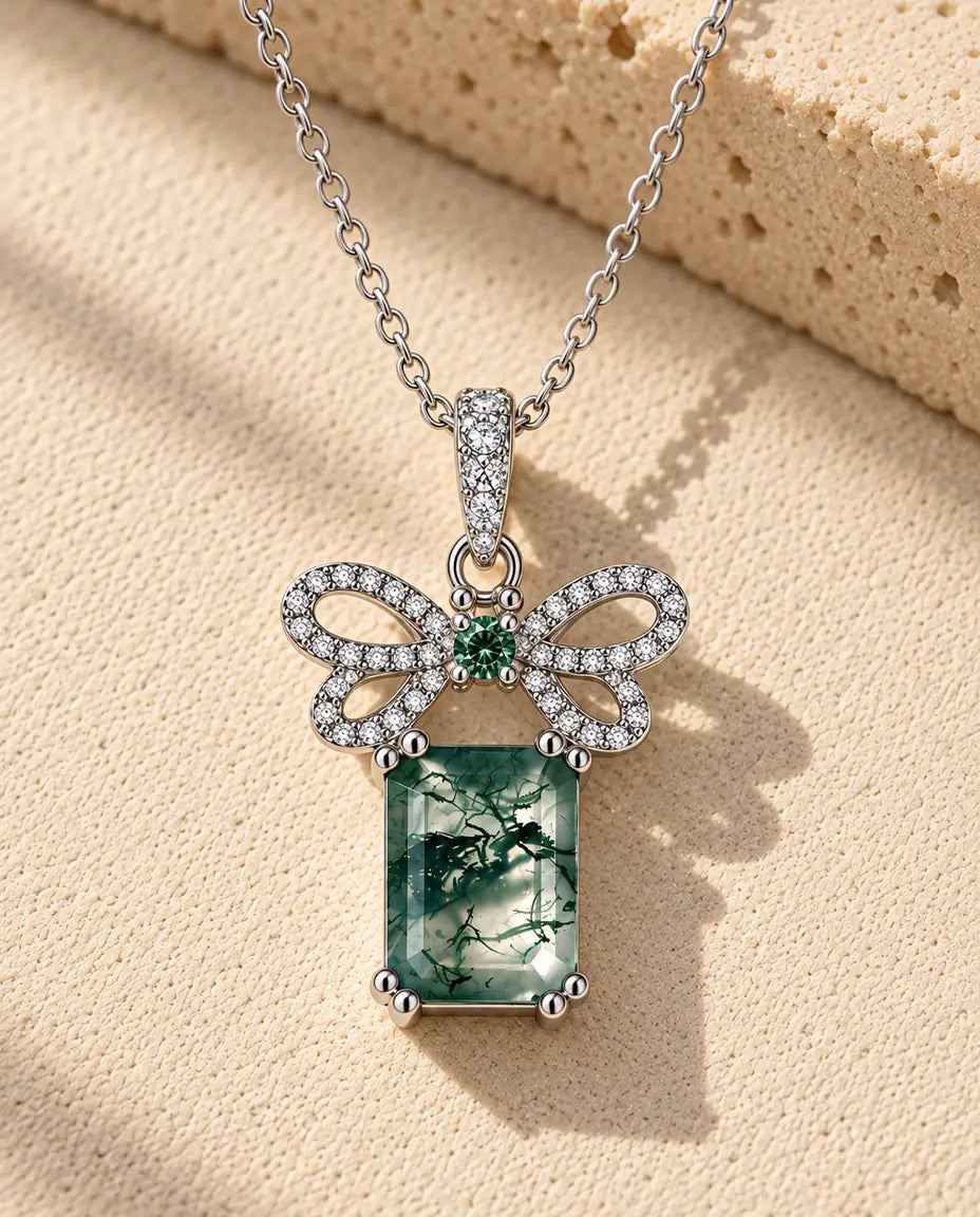 Moss Agate Bow Necklace in 925 Sterling Silver - lying on a cream textured surface beside a travertine block
