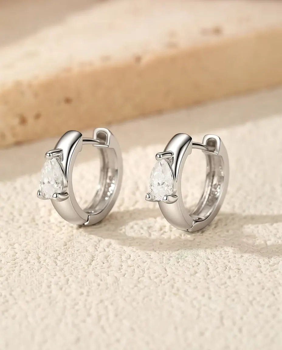 Pear Moissanite Huggie Hoop Earrings in 925 Sterling Silver - the pair standing side by side on a cream textured surface