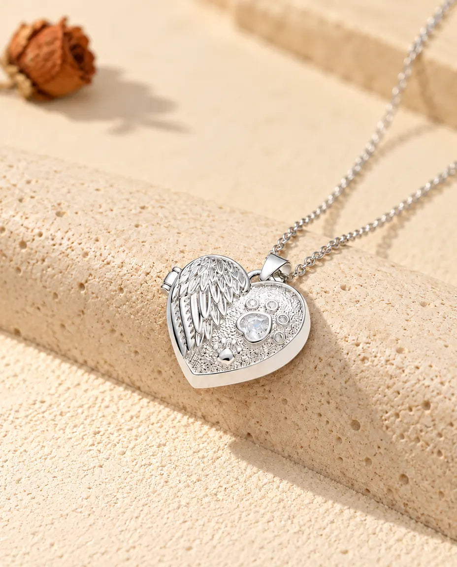 Personalised angel wing paw print heart photo locket necklace in silver tone with a heart-shaped stone paw print, resting on a travertine block