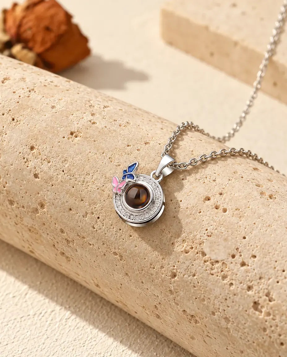 Personalised butterfly circle photo projection necklace in silver tone with navy and pink enamel butterflies, on travertine