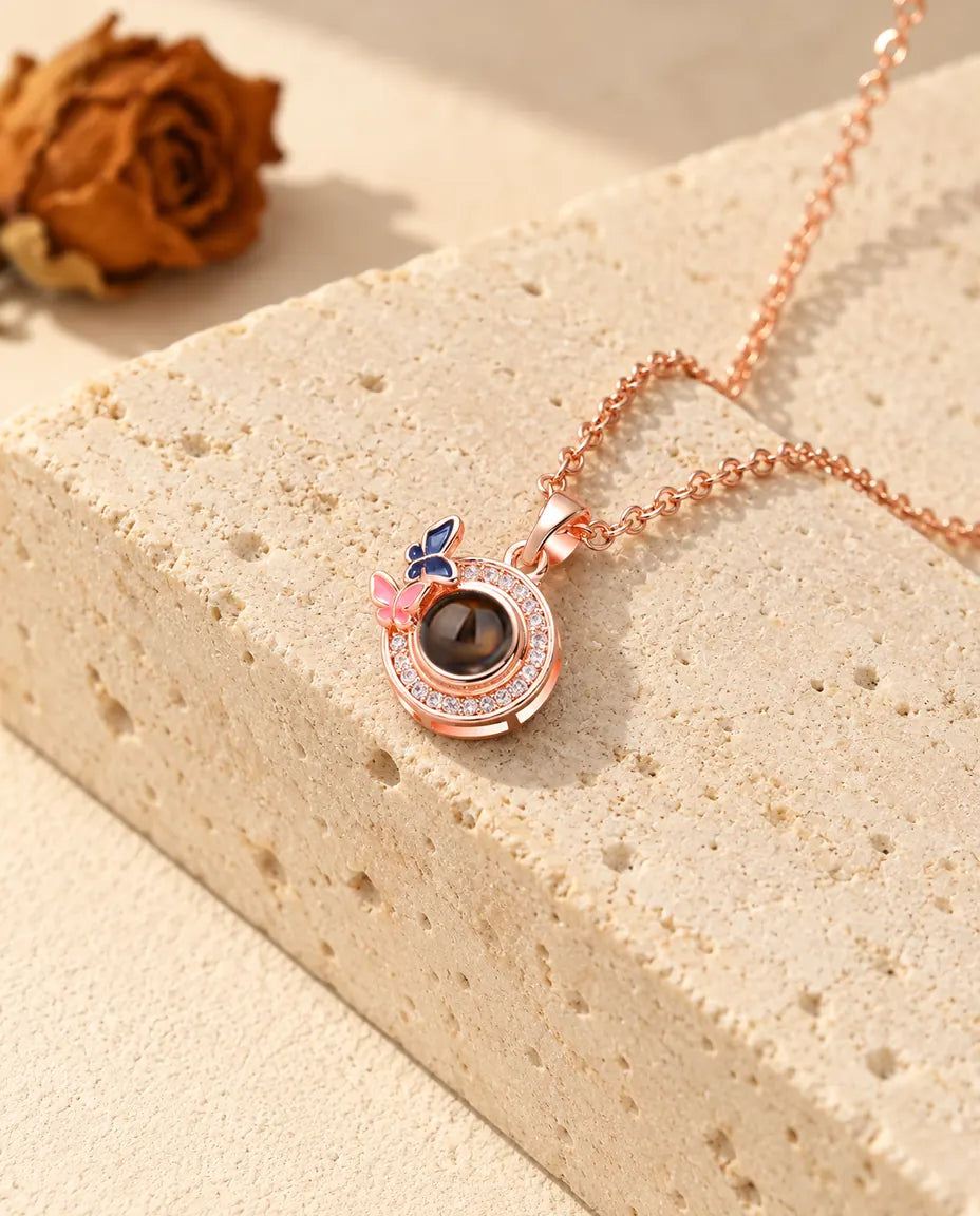 Rose gold tone halo circle pendant with two enamel butterflies resting against a travertine block
