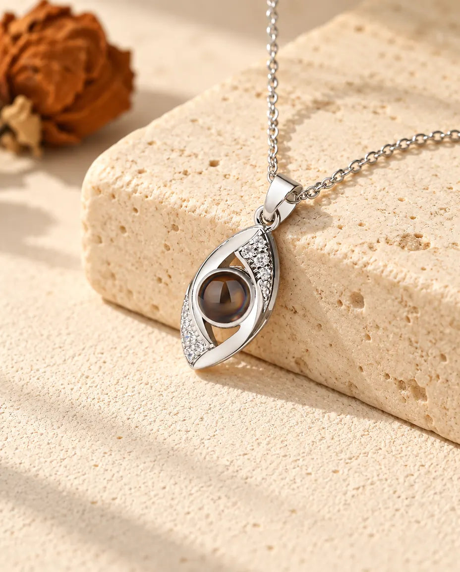 Personalised silver tone evil eye photo projection necklace lying over a travertine block