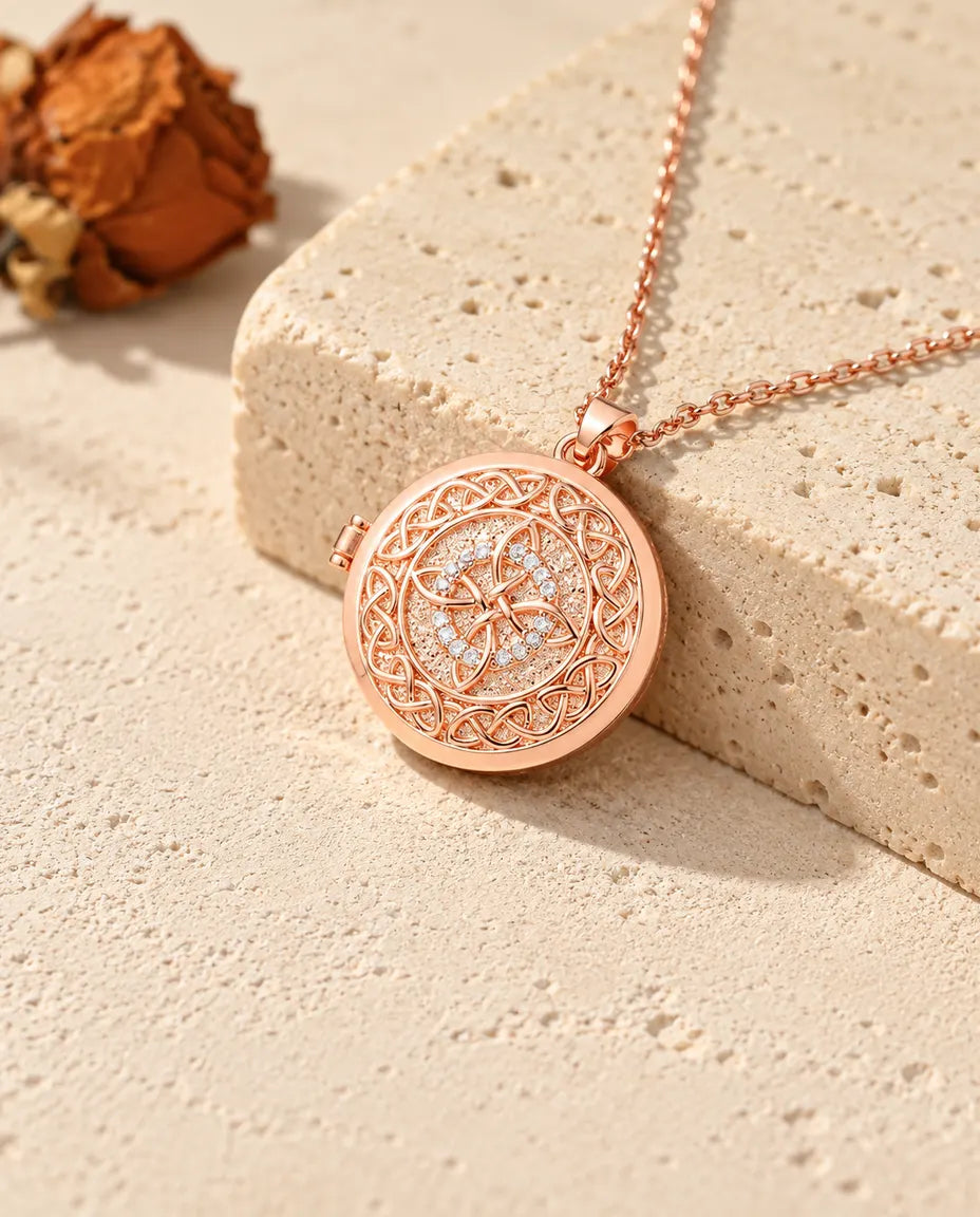 Rose gold tone four-loop Celtic knot photo locket necklace on travertine in warm sunlight