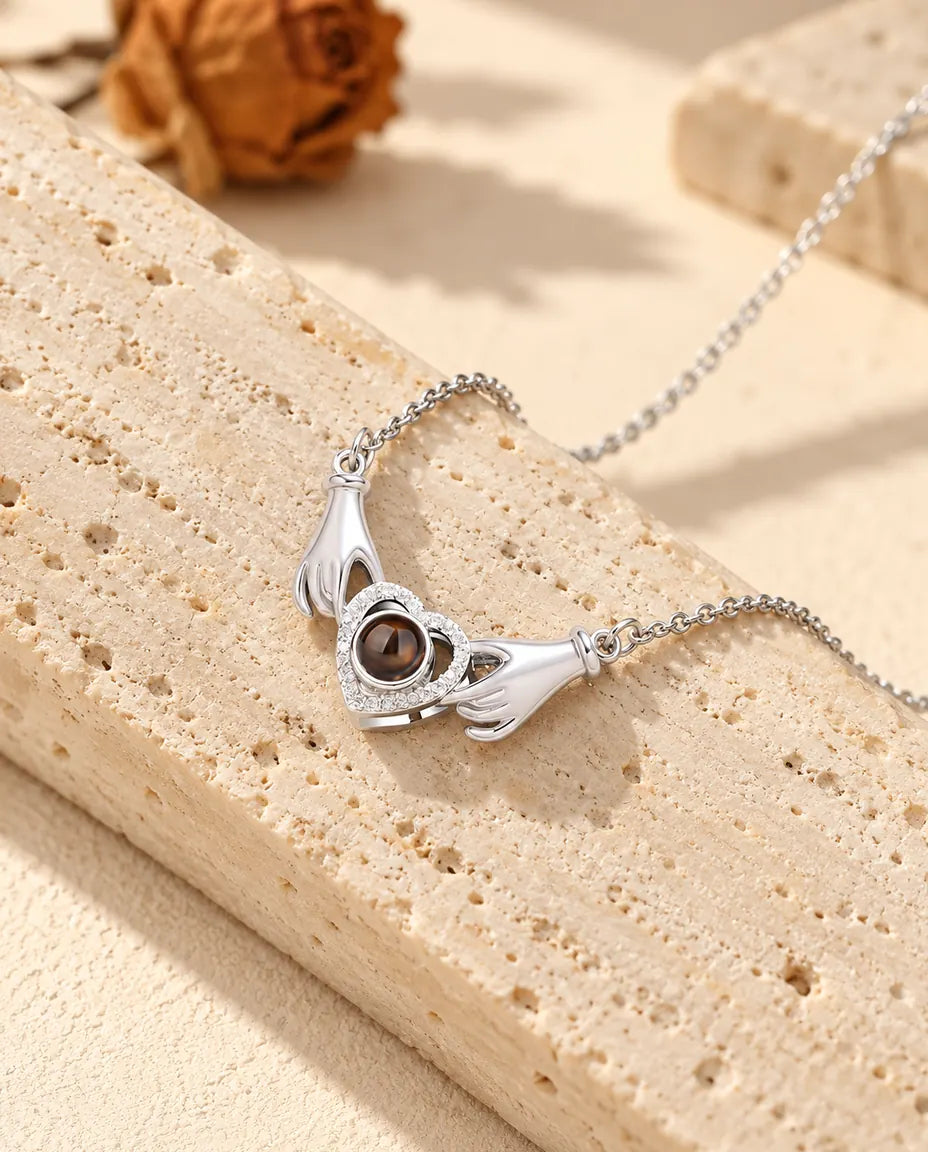 Personalised photo projection necklace in silver with two little hands holding a pave heart, resting on a travertine block