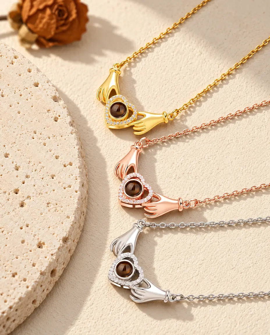 Gold tone, rose gold tone and silver hands holding heart necklaces stacked beside a travertine slab