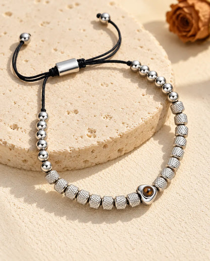 Personalised heart photo projection beaded bracelet in silver tone with textured barrel beads, on a travertine slab