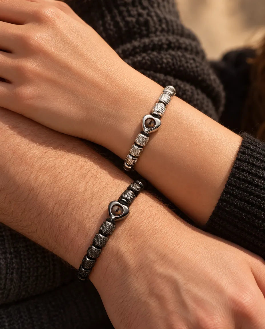 Close-up of his and her wrists side by side with matching silver tone and black heart bead bracelets