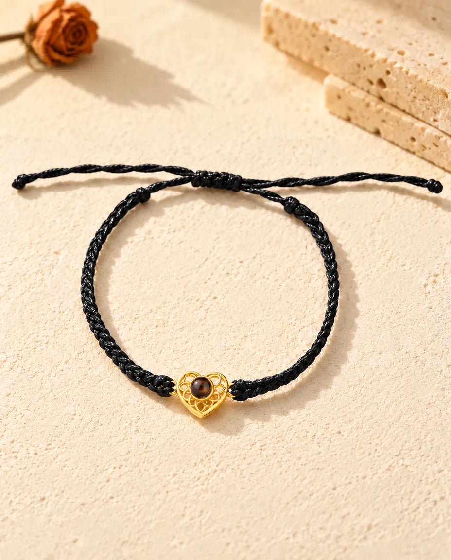 Top view of the gold tone heart charm bracelet on a black thin braided cord with its sliding knot and cord ends