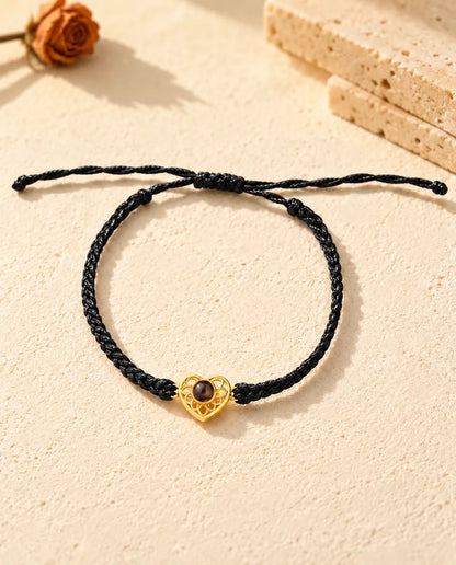 Top view of the gold tone heart charm bracelet on a black thin braided cord with its sliding knot and cord ends