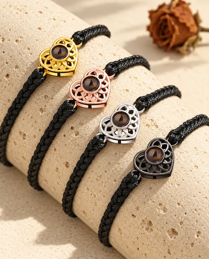 Four black thin braided cord bracelets showing every charm colour draped over travertine