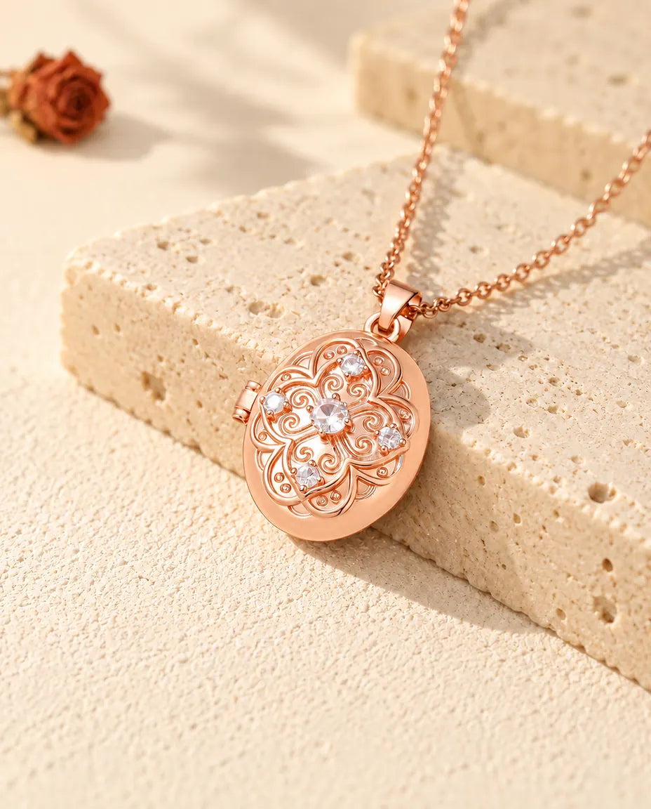 Rose gold tone oval photo locket with a cubic zirconia flower lid resting on travertine