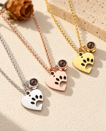 Three colours of the paw print heart pet projection necklace on a diagonal on cream plaster