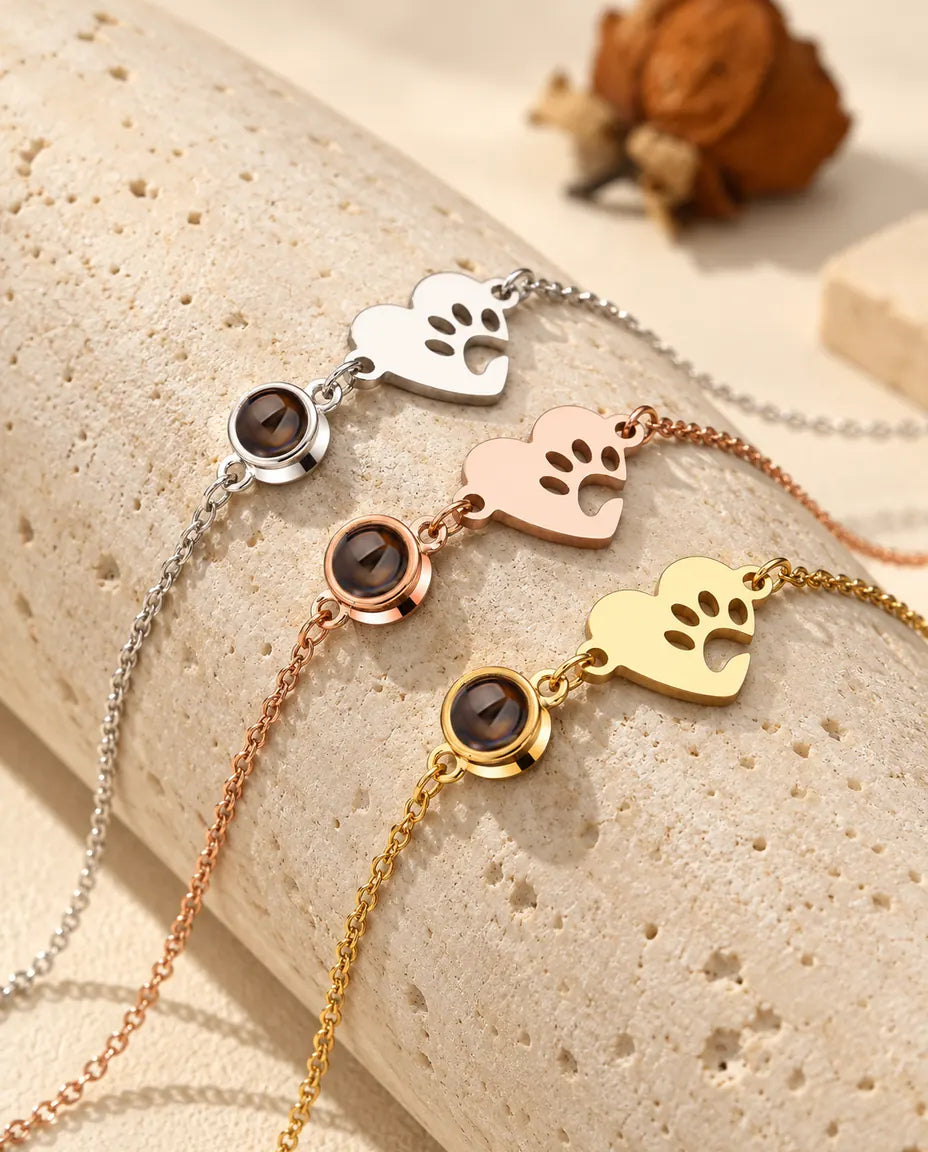 Three paw print heart projection bracelets in silver tone, rose gold tone and gold tone over a travertine block