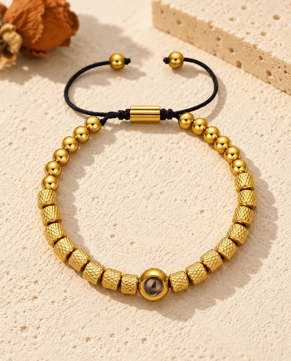 Personalised photo projection bead bracelet in gold tone with textured barrel beads and a sliding cord, on cream plaster