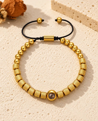 Personalised photo projection bead bracelet in gold tone with textured barrel beads and a sliding cord, on cream plaster