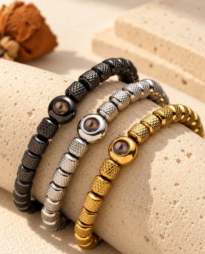 Three bead bracelets in black, silver tone and gold tone draped over a travertine block