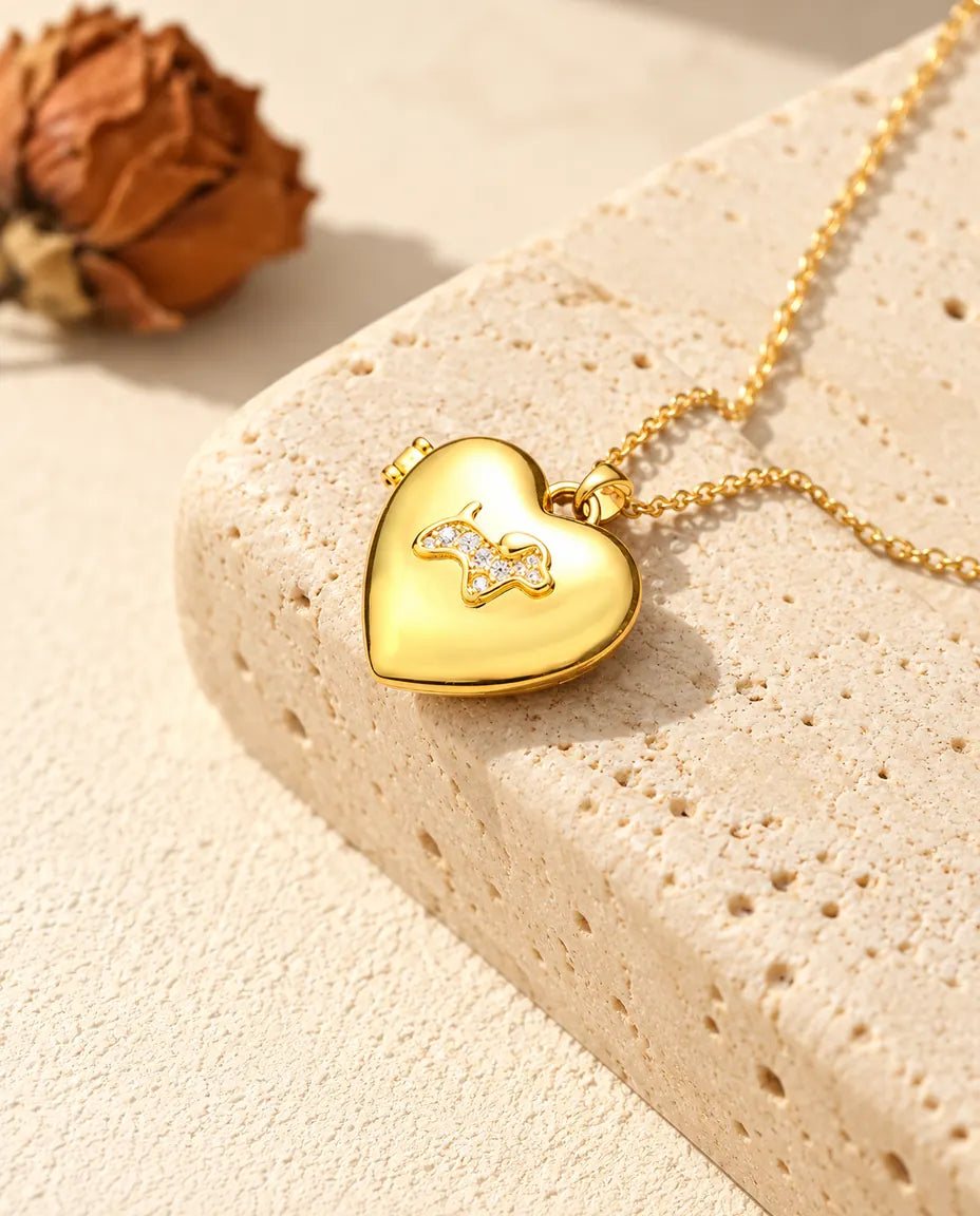 Gold tone puppy heart photo locket necklace resting on a travertine block
