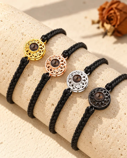 Four black thin braided cord bracelets showing every charm colour draped over travertine