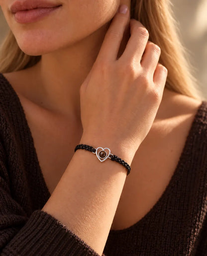 Woman with her fingertips at the side of her neck wearing the silver open heart bracelet on a black cord