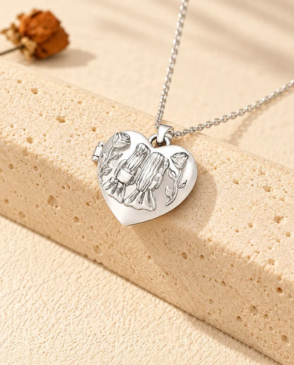 Personalised sisters heart photo locket necklace in silver tone with two girls and roses on the lid, resting on a travertine block