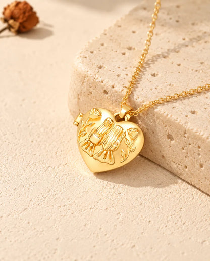 Gold tone sisters heart photo locket necklace resting on a travertine block