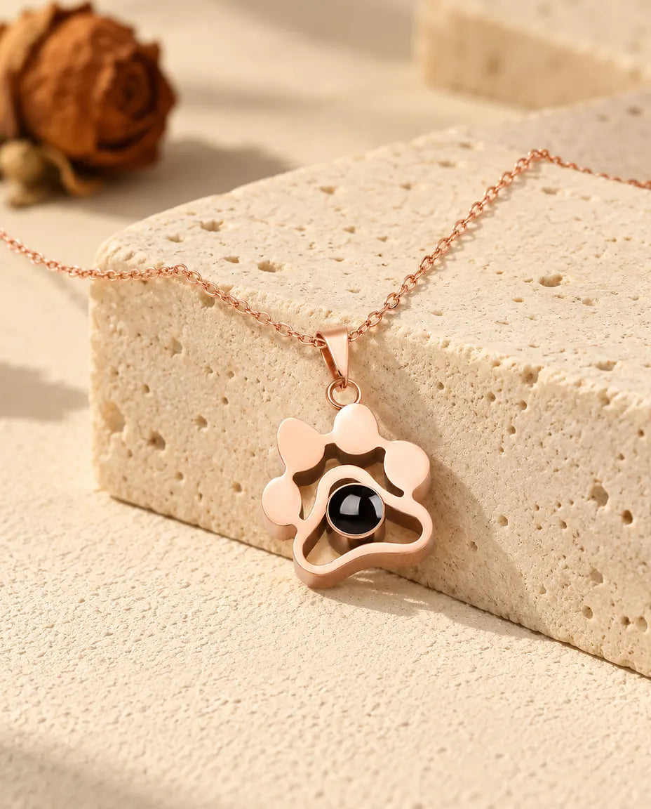 Rose gold tone paw print projection necklace draped over a travertine block