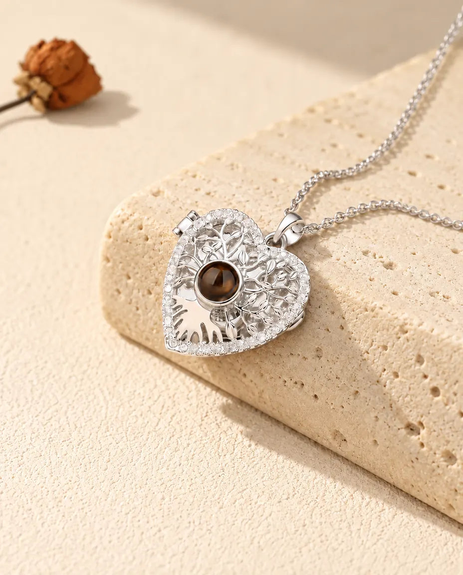 Personalised tree of life heart locket necklace in silver tone with a brown projection stone, resting on a travertine block