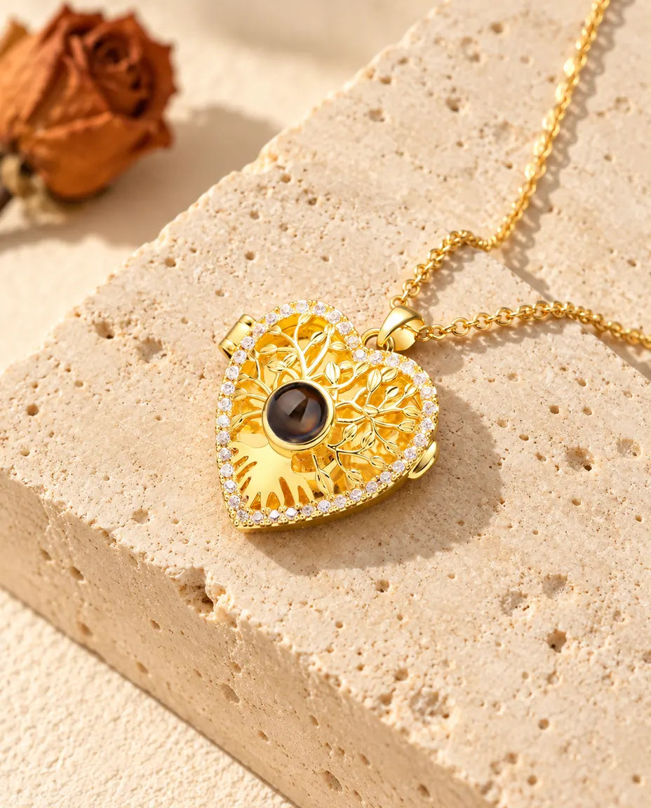 Gold tone heart locket with an openwork tree of life and a cubic zirconia outline resting on travertine