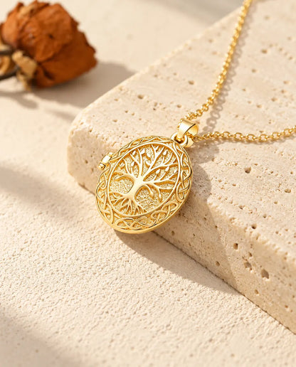 Gold tone oval tree of life locket necklace draped over a travertine block