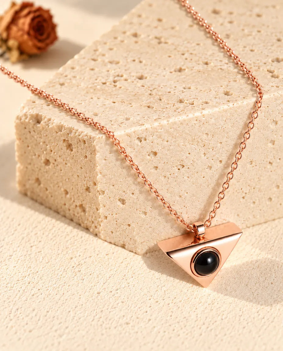 Rose gold tone triangle projection necklace hanging over a travertine block