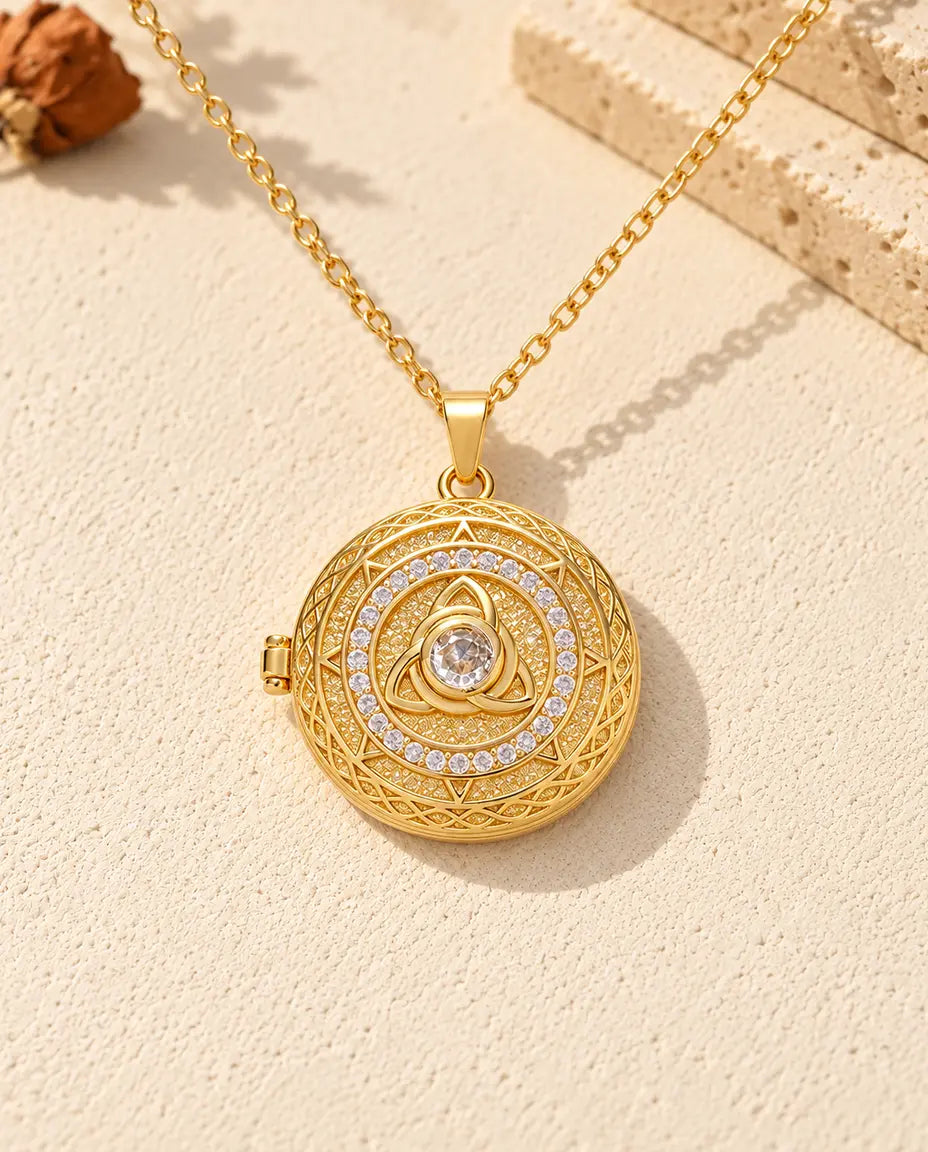 Front view of the gold tone round locket showing the trinity knot, centre stone, stone circle and side hinge