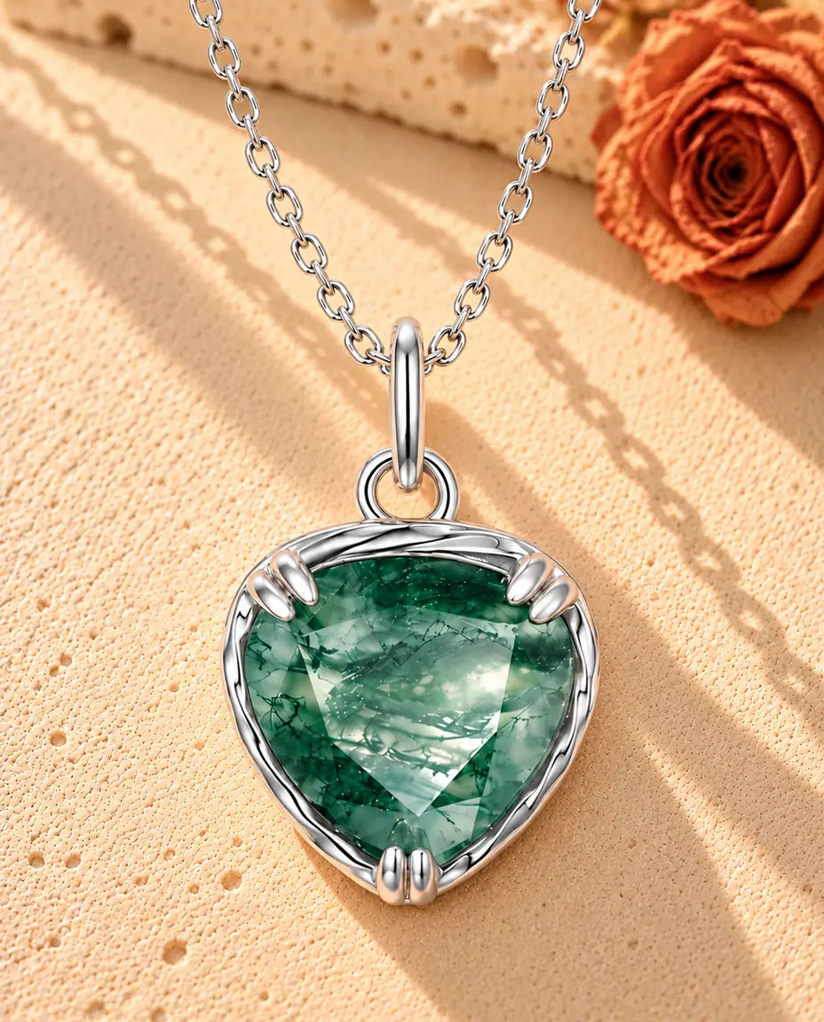 Heart Moss Agate Pendant Necklace in 925 Sterling Silver - lying on a cream textured surface beside a travertine block